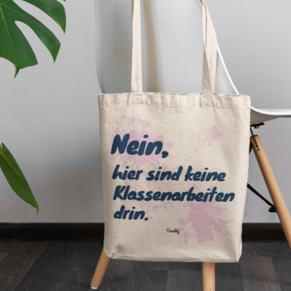 Die Teachly Bio-Baumwoll Tasche mit lustigem Nein, hier sind keine Klassenarbeiten drin Motiv und Rosa Design für Lehrerinnen und Lehrer um einen Stuhl gehangen